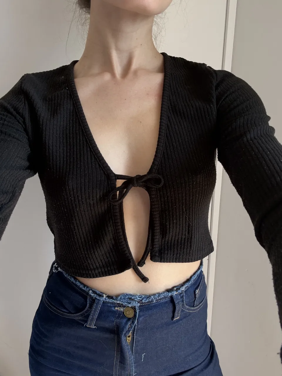 Top negro de H&M, escote en V con lazo, manga larga y corte al cuerpo. Ideal para un look canchero y moderno.