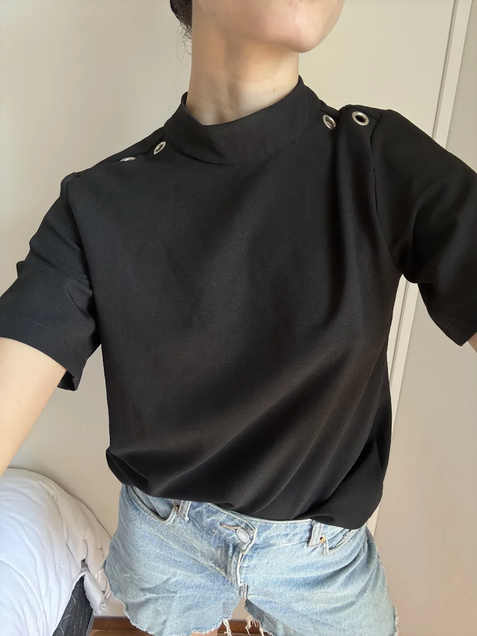 Remera negra de cuello alto con detalles de ojales plateados en los hombros. Manga corta. Ideal para un look moderno y sofisticado.
