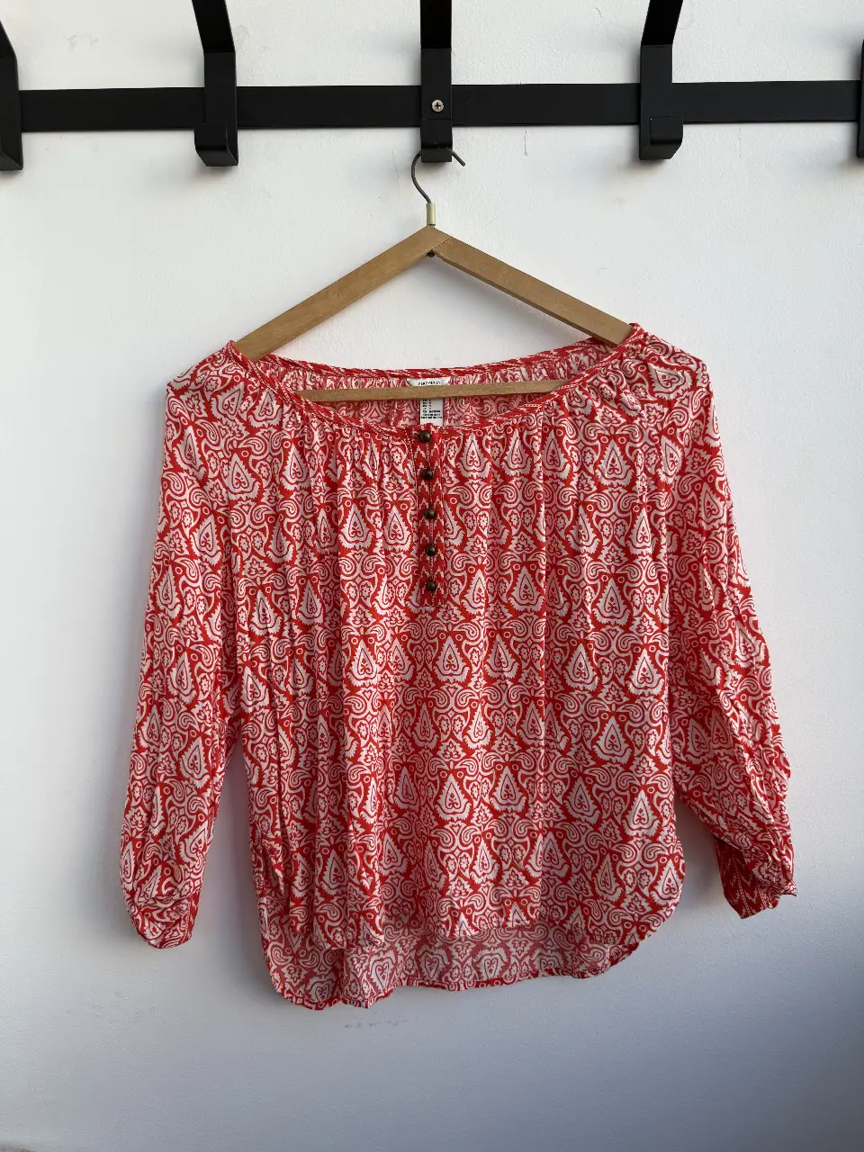 Blusa de mujer con estampado paisley en rojo y blanco. Tiene mangas 3/4 con botones en los puños y botones en la parte delantera. Ideal para un look casual y cómodo.