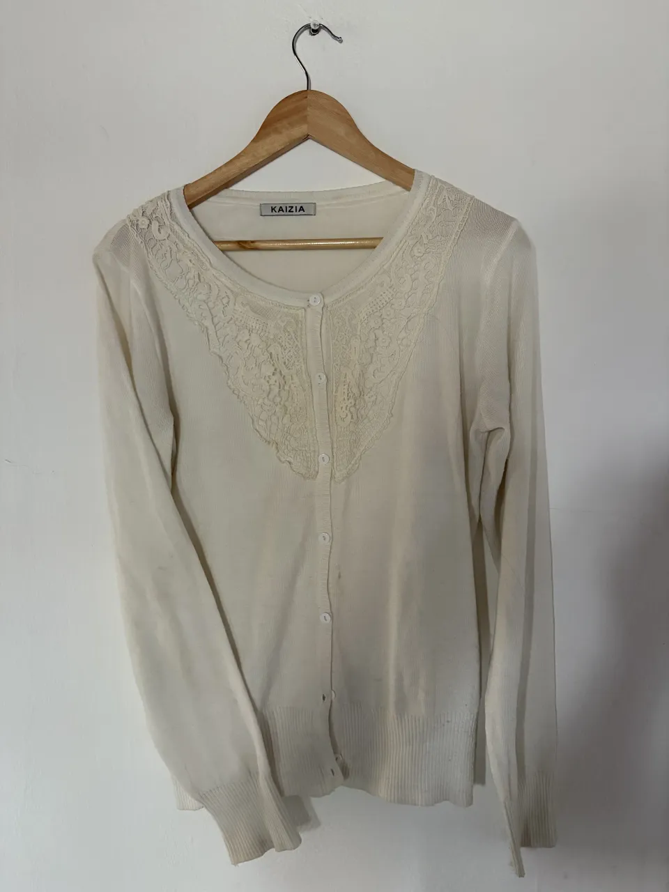 Cardigan blanco de hilo con detalles de encaje en el cuello y botones al frente. Manga larga y puños elastizados.