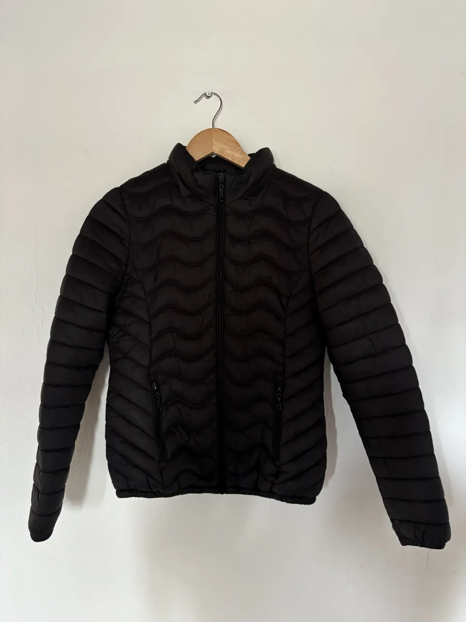 Campera acolchada negra con cuello alto y cierre. Posee bolsillos con cierre a los costados. Ideal para el frío y para un look casual.