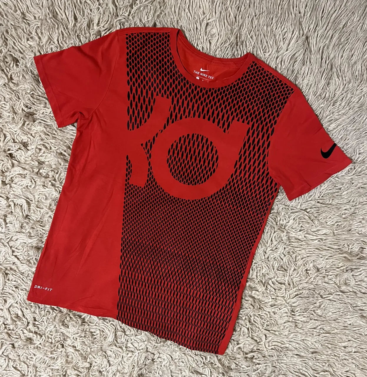 Remera deportiva roja con estampa negra al frente del logo 'KD' y detalles de puntos. Posee la tecnología Dri-Fit y el logo de Nike en la manga.