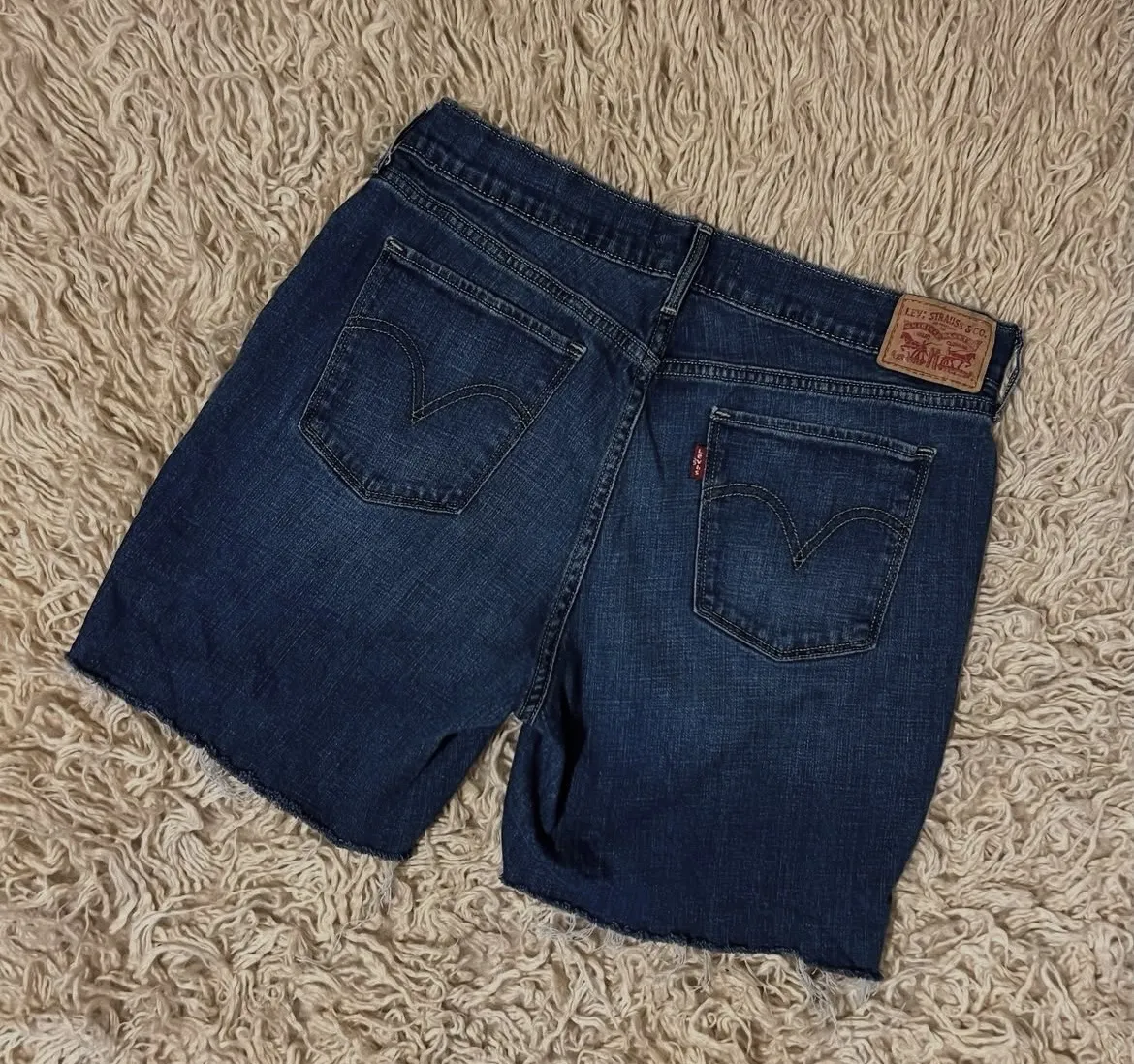 Shorts de jean azul oscuro con roturas deshilachadas en el borde inferior. Presentan bolsillos delanteros y traseros, y el clásico detalle de la marca en los bolsillos traseros. cintura 38 Cm - Largo 41 Cm 