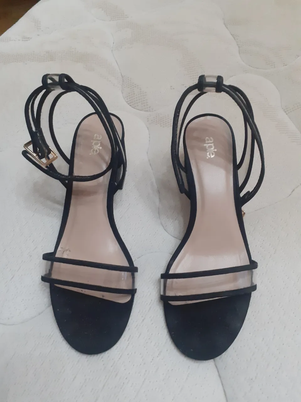 Sandalias negras con tiras finas transparentes y detalle de hebilla dorada. Perfectas para un look elegante y moderno.