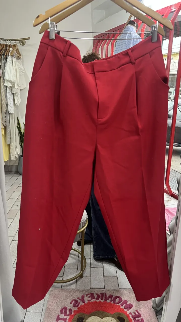 Pantalón rojo de vestir con bolsillos delanteros y traseros. Tiene pinzas en la parte delantera y cierre con botón y gancho.