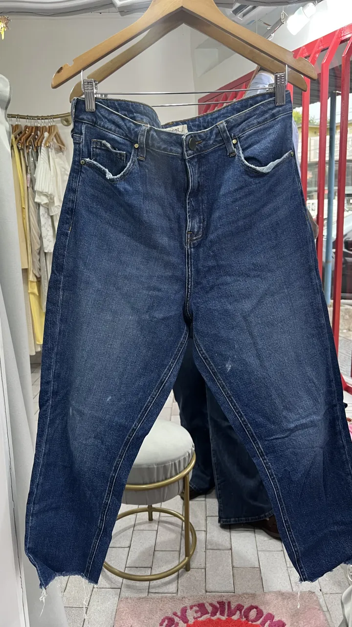 Jeans de corte recto, color azul. Tienen roturas en los bordes inferiores y detalles desgastados. está manchado y roto en los bolsillos 