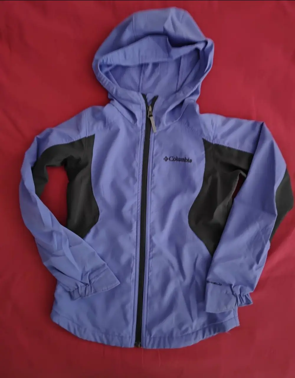 Campera deportiva Columbia para niña, color violeta con detalles en gris. Con capucha y cierre frontal. Ideal para actividades al aire libre.