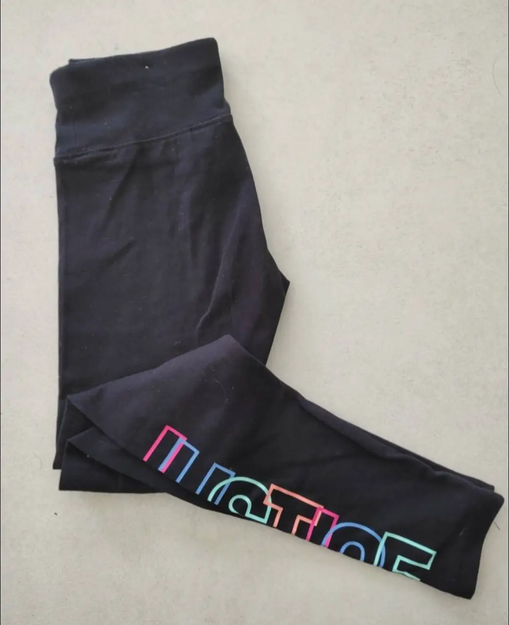 Calzas deportivas negras con estampado de la palabra "JUSTICE" en colores vibrantes. Ideales para actividades físicas o un look casual.