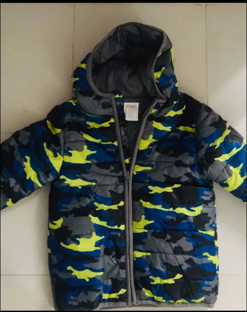 Campera de abrigo para niño con diseño de camuflaje en tonos grises, azules y detalles en amarillo. Posee capucha y cierre frontal. Ideal para el invierno.