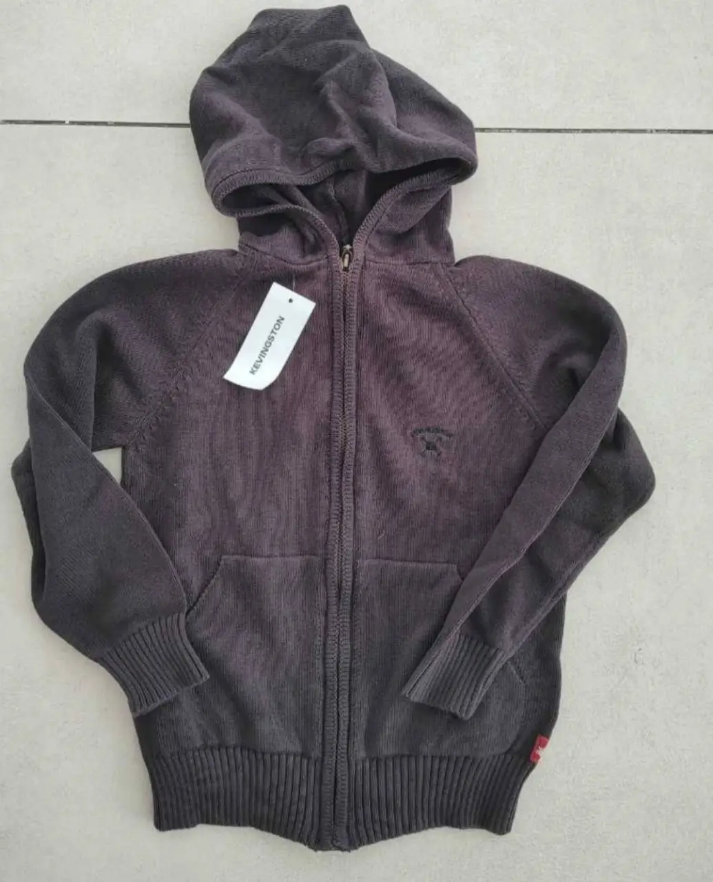 Buzo con cierre y capucha, de color gris oscuro, con etiqueta de la marca KEVINGSTON. Ideal para un look casual y abrigado.
