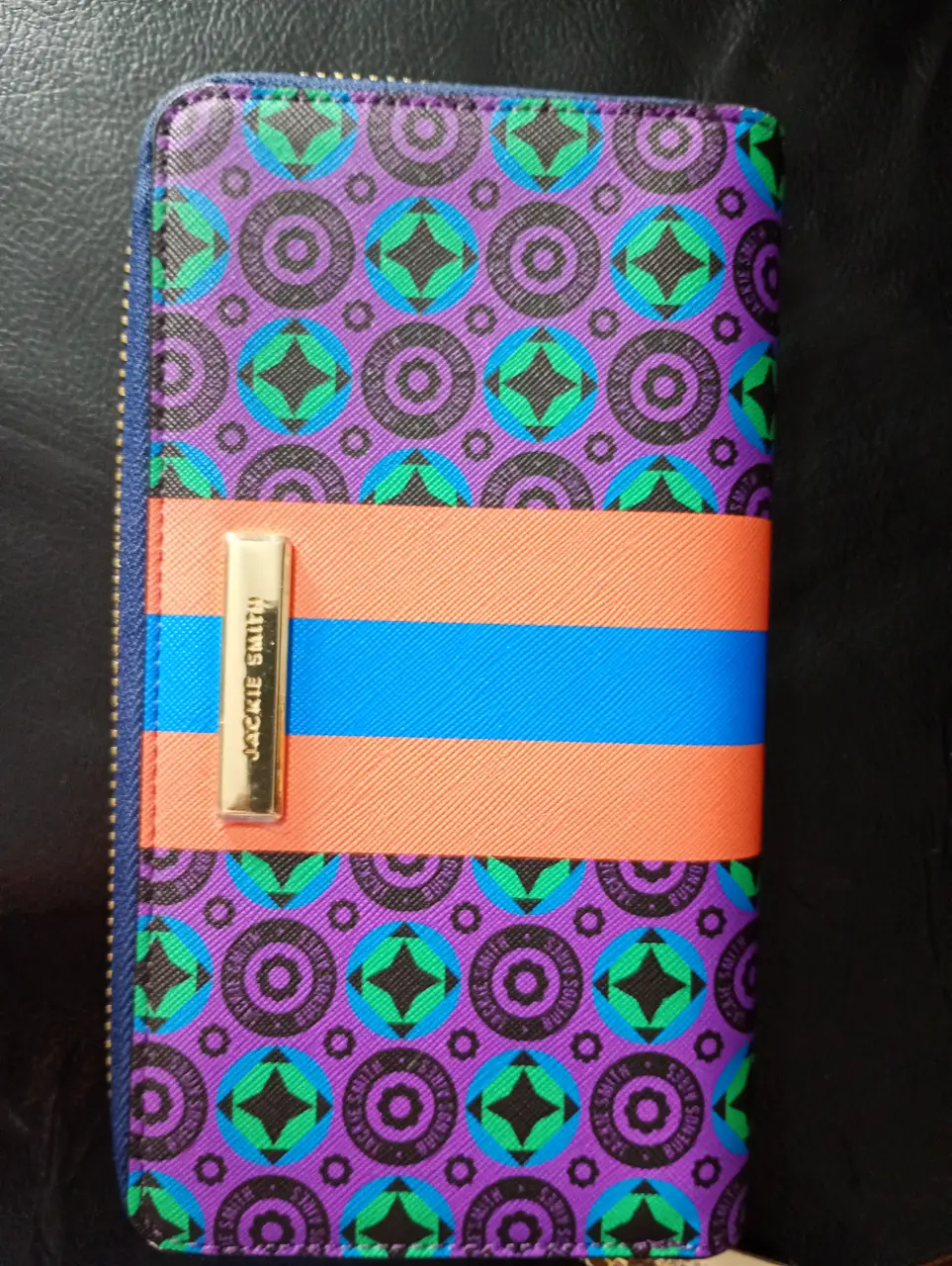 Billetera SIN USO  Jackie Smith con diseño geométrico en tonos violeta, naranja y azul. Cuenta con cierre y detalles dorados.