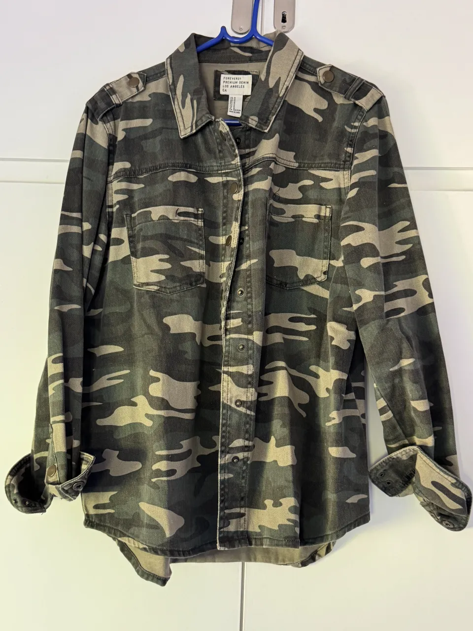 Camisa de manga larga con estampa camuflada en tonos verdes y grises. Posee cuello, cierre con botones a presión en el frente y dos bolsillos en el pecho. 