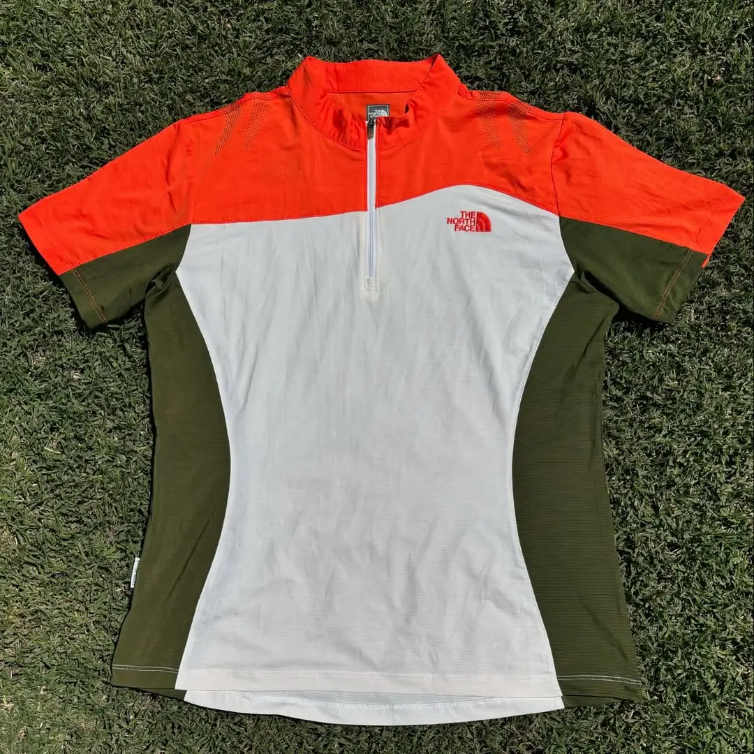 Remera deportiva The North Face para hombre/mujer, manga corta, con cierre en el cuello. Combina naranja, blanco y verde. Ideal para actividades al aire libre. Secado rápido, Ancho 52cm/ Largo 64cm. Talle XL (dama) o Talle M (hombre)