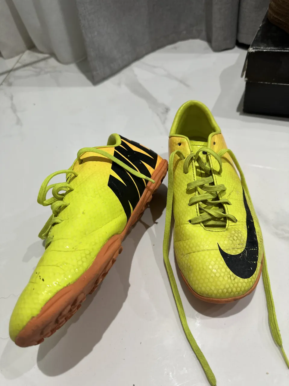 Zapatillas de fútbol para césped sintético, color amarillo con detalles en negro y suela naranja.