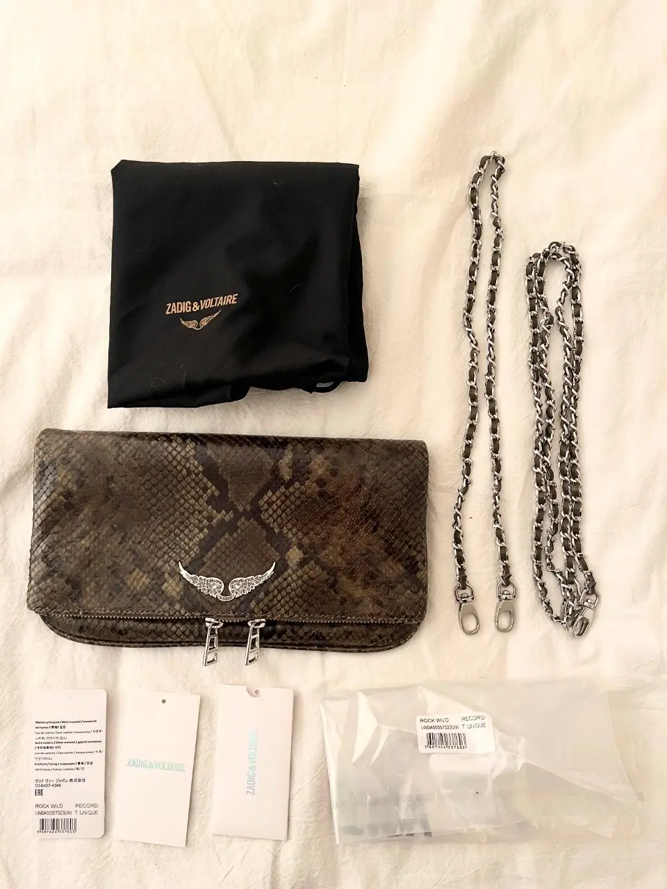 Cartera sobre de mano de cuero con estampado de serpiente, cierre metálico y cadena para colgar. Incluye bolsa protectora y etiquetas.