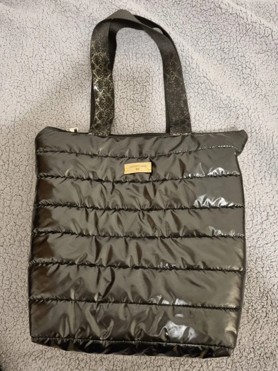 Bolso tote negro acolchado con manijas y detalles dorados. Ideal para llevar todo lo necesario con estilo.