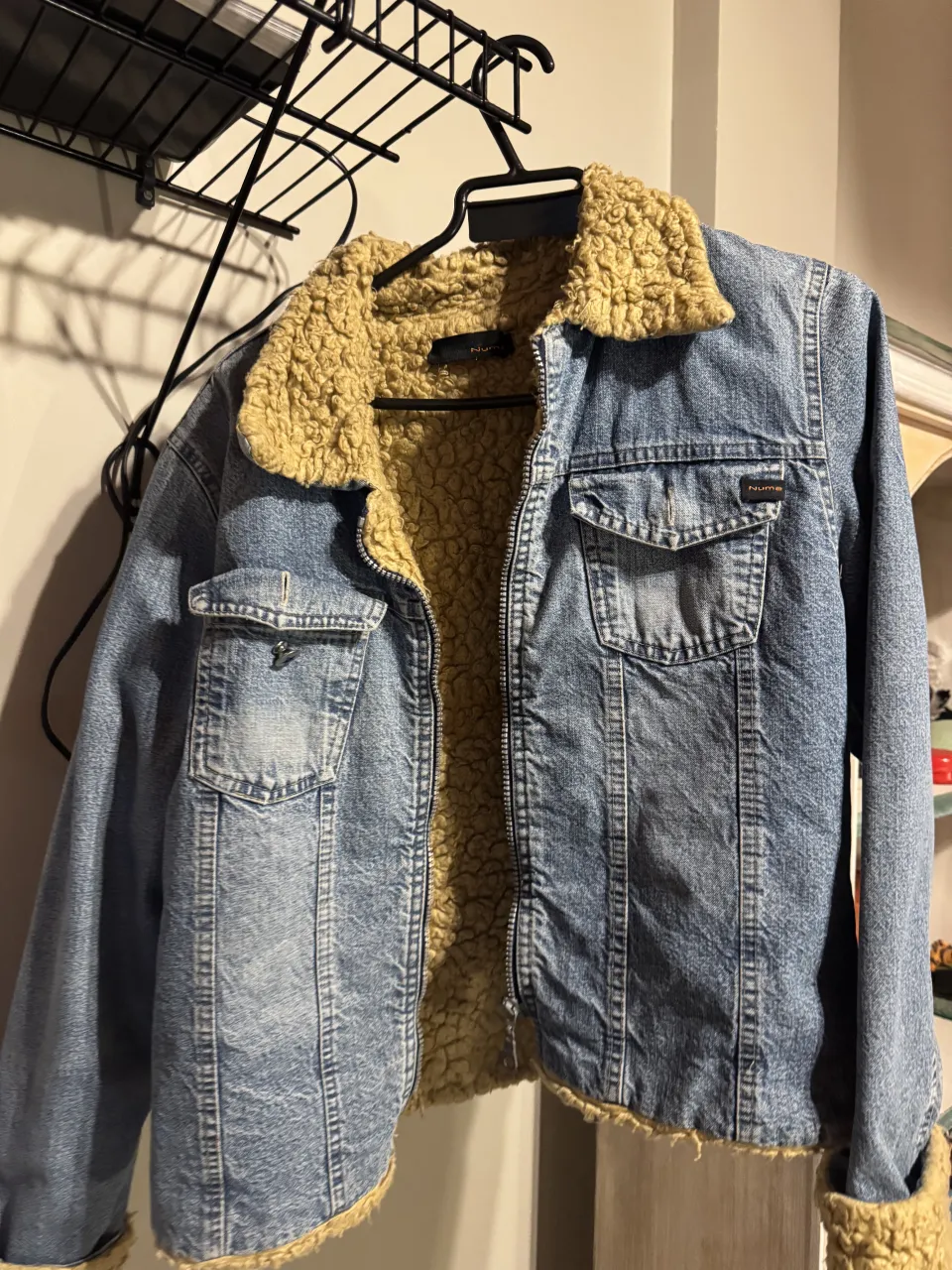Campera de jean azul con forro y cuello de corderito color crudo. Tiene bolsillos con solapa en el frente y cierre.