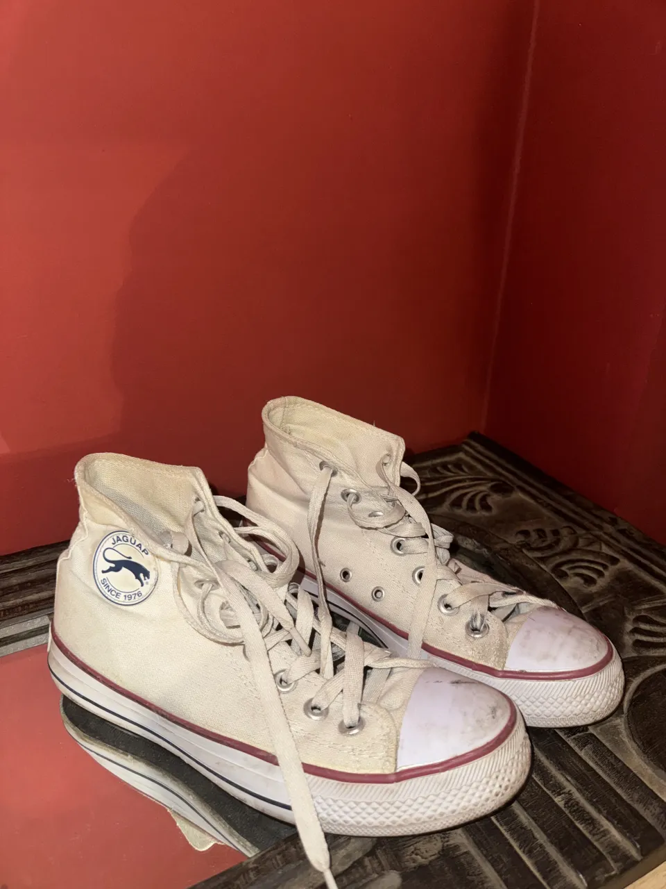 Zapatillas de lona color blanco, modelo de caña alta con cordones. Presentan detalles en color rojo en la suela y el logo de la marca en el lateral.