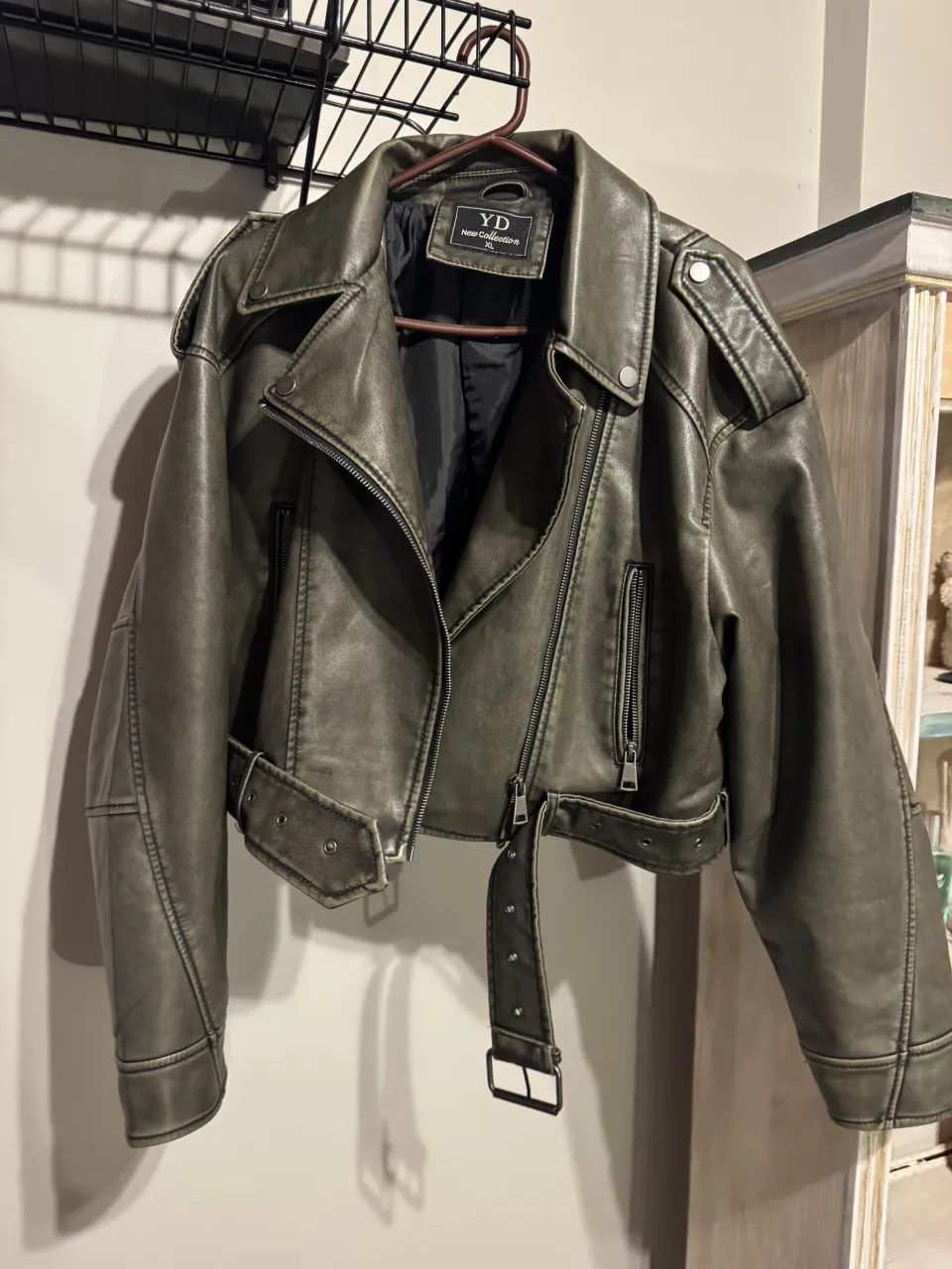 Campera de cuero sintético, estilo biker, con cuello solapa, cierre al frente y en bolsillos, y cinturón con hebilla.