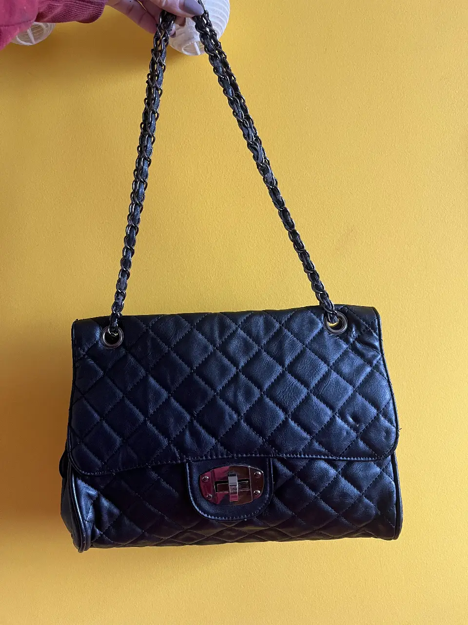 Cartera negra acolchada de cuero ecológico con cadena y cierre de metal. Tiene detalles en la correa (desprendimiento del material por el paso del tiempo)