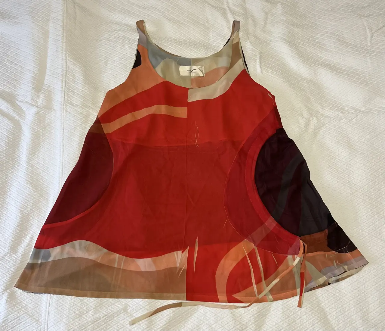 Top de mujer con estampado abstracto en tonos rojos, naranjas, marrones y negros. Diseño con tirantes finos y detalles de lazos en la parte inferior. Ideal para un look moderno y llamativo.