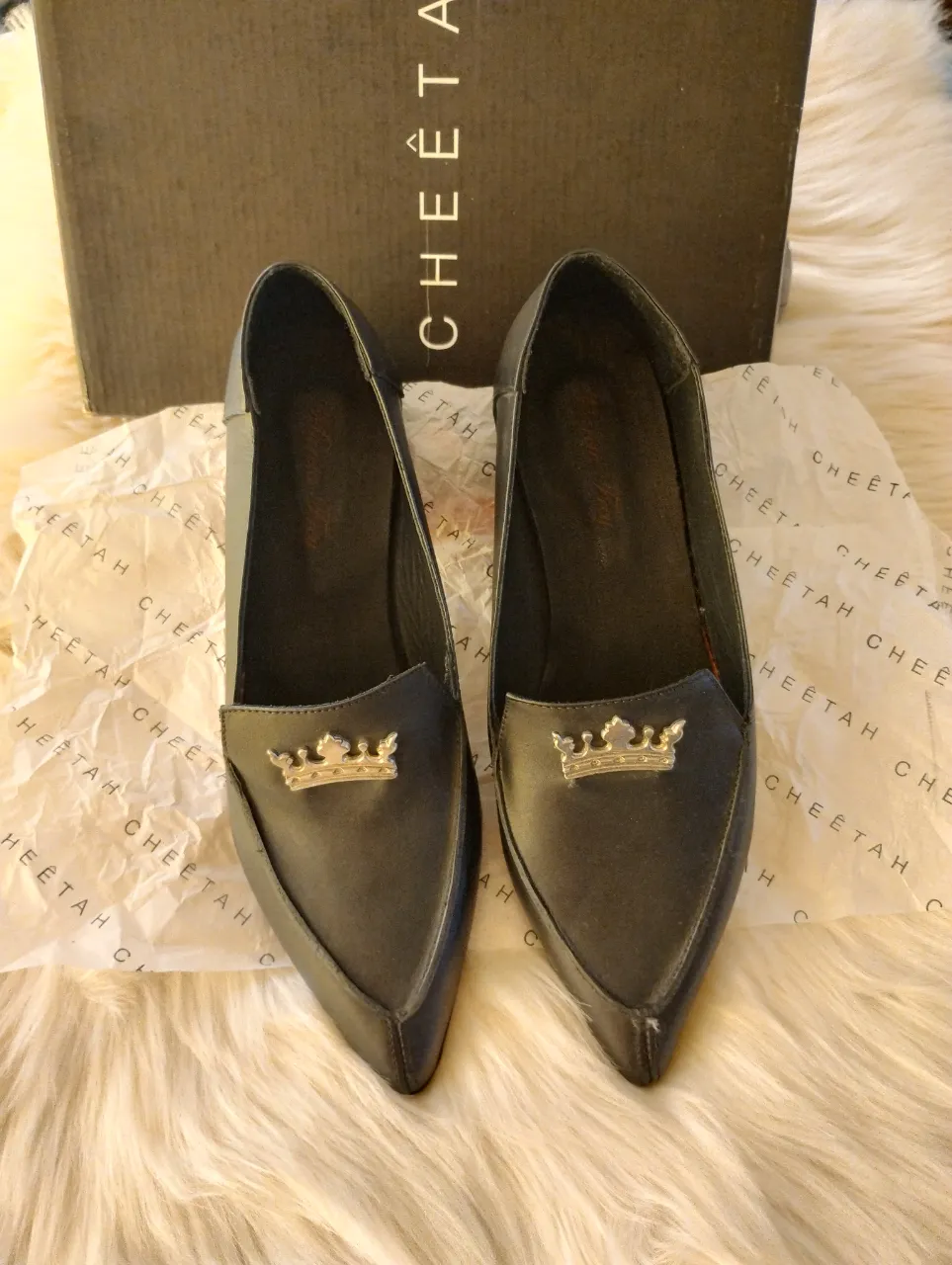 Zapatos negros con punta fina y detalle de corona dorada en la capellada.