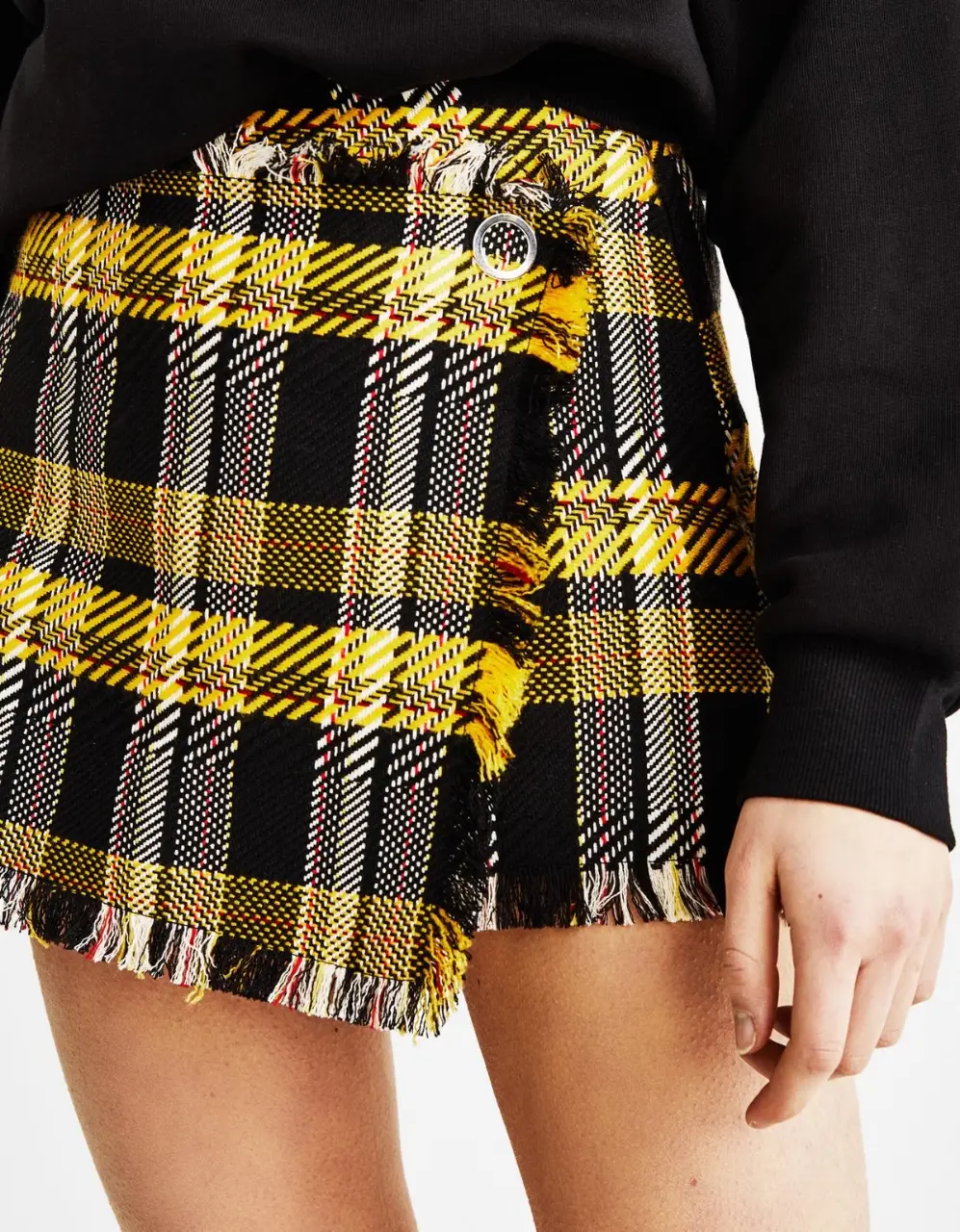 Pollera short de tela escocesa lanilla, en tonos amarillo y negro con flecos en el borde. Ideal para un look casual y moderno en Invierno y media estación. Cierre invisible en lateral.