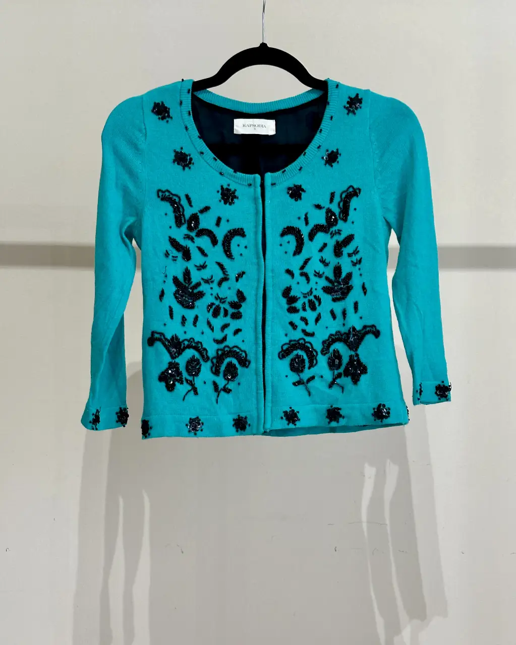 Cardigan saco de mujer turquesa con bordados en negro. Ideal para un look elegante y sofisticado. Mangas 3/4. Se prende adelante con pequeños brochecitos tipo lenceros. Es ideal para usarlo sobre la piel ya que es de Excelente calidad y no pica, o sea una remera básica debajo.