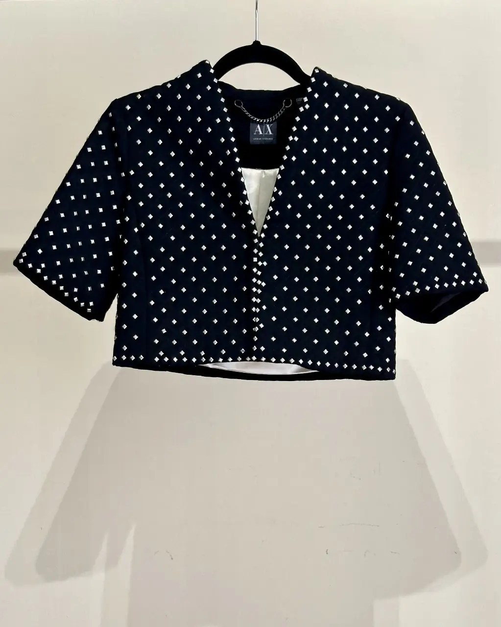 Chaqueta negra con tachas plateadas en toda la superficie, estilo blazer corto con cuello en V y mangas cortas. Ideal para un look elegante y moderno. Impecable.