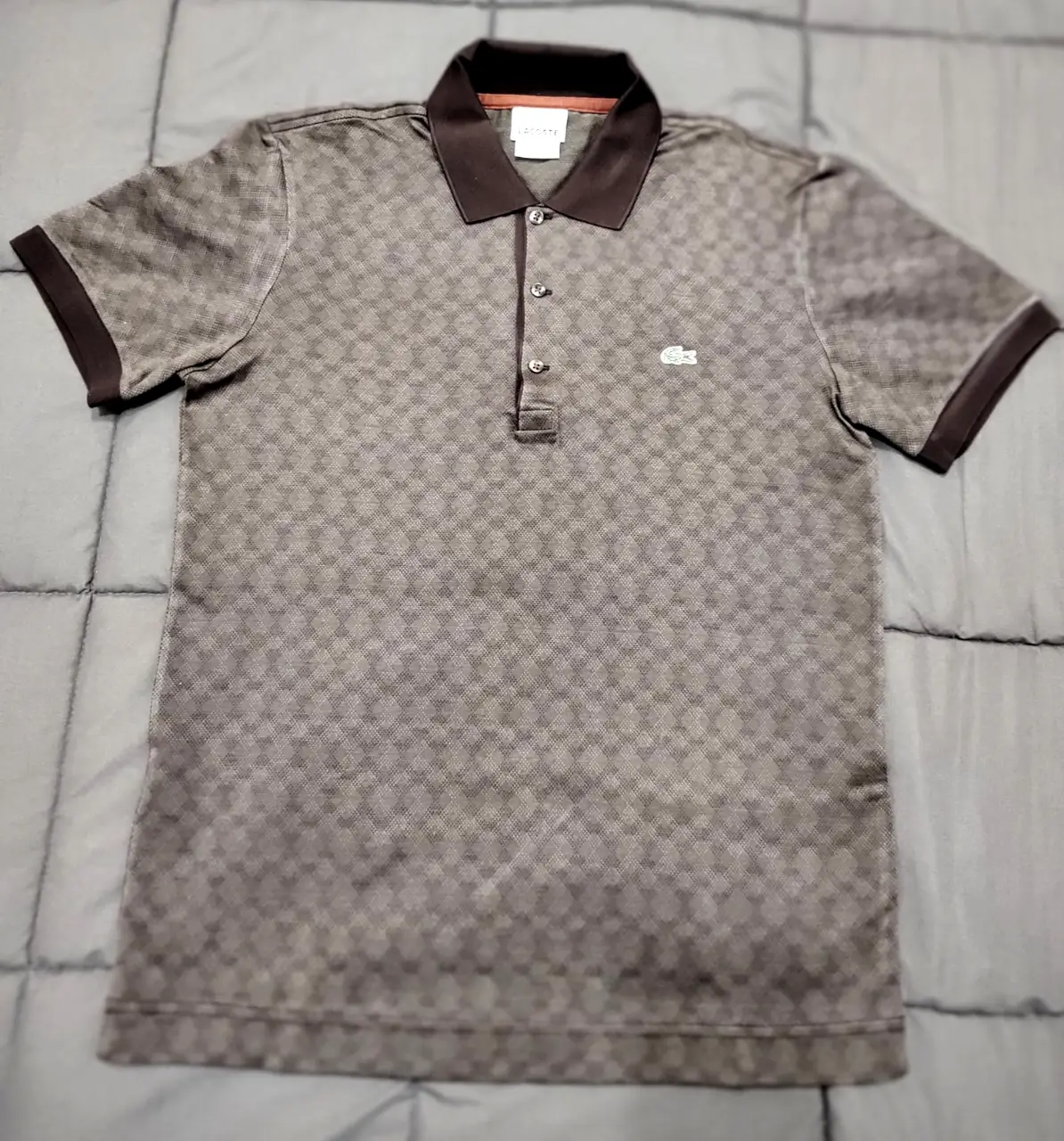 Remera polo Lacoste para hombre, con diseño de cuadros en tonos marrones. Cuello y mangas con detalles en marrón oscuro. Ideal para un look casual y elegante.