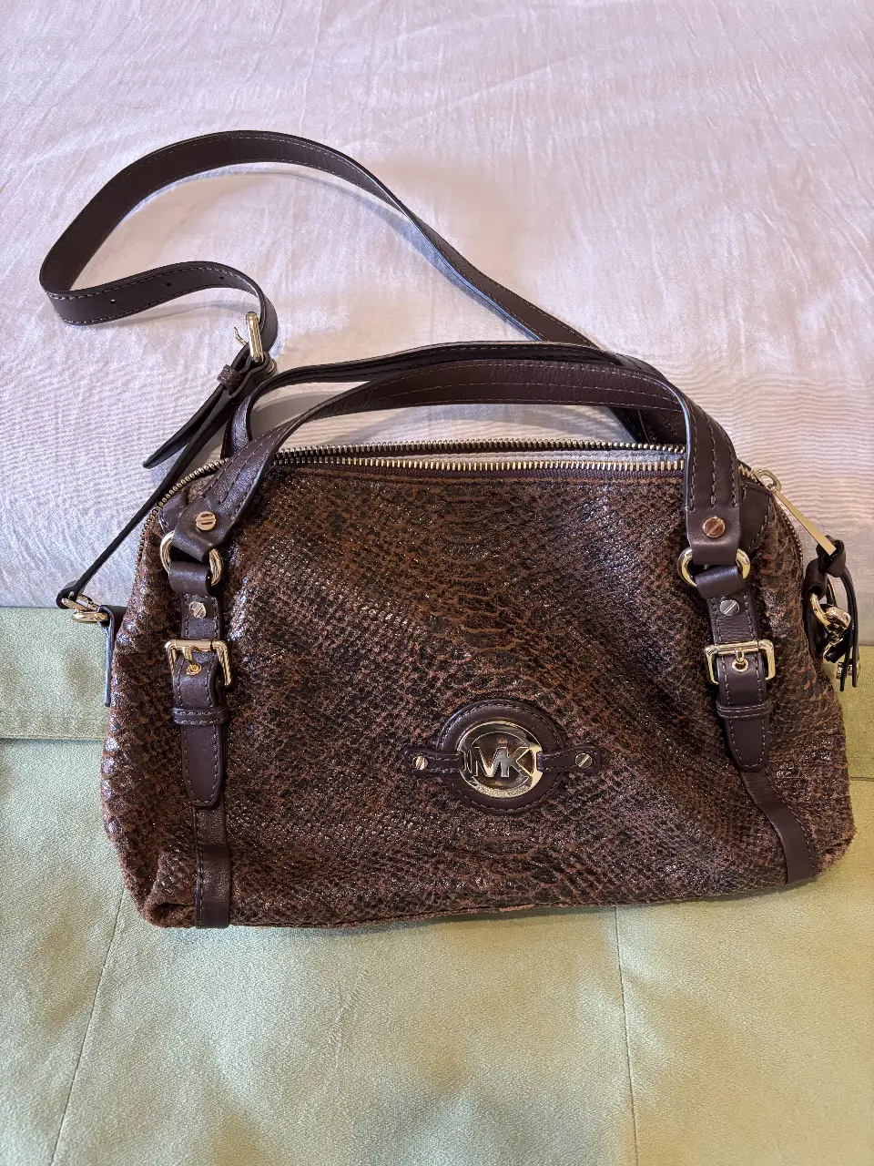Cartera Michael Kors de hombro, marrón con textura símil piel de serpiente. Detalles dorados y logo de la marca en el frente. Ideal para un look elegante y sofisticado.