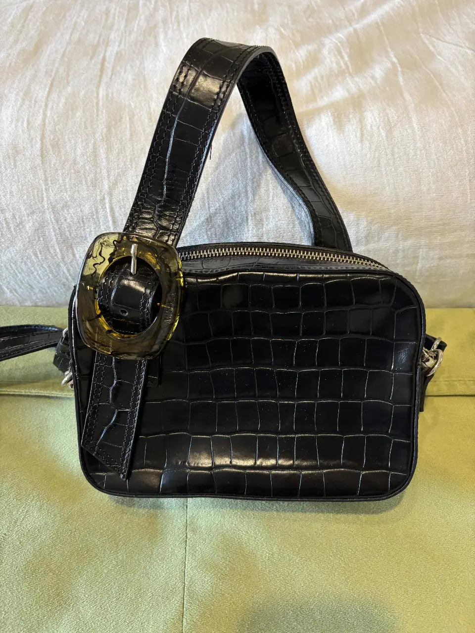 Cartera negra con textura de cocodrilo, con manija superior y detalle de hebilla transparente. Ideal para un look elegante y moderno.