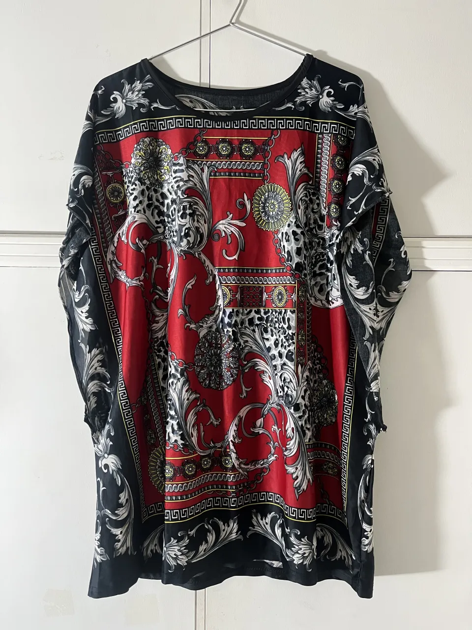 Remera estampada con diseño barroco en rojo, negro y detalles dorados y plateados. Posee cuello redondo y mangas largas.