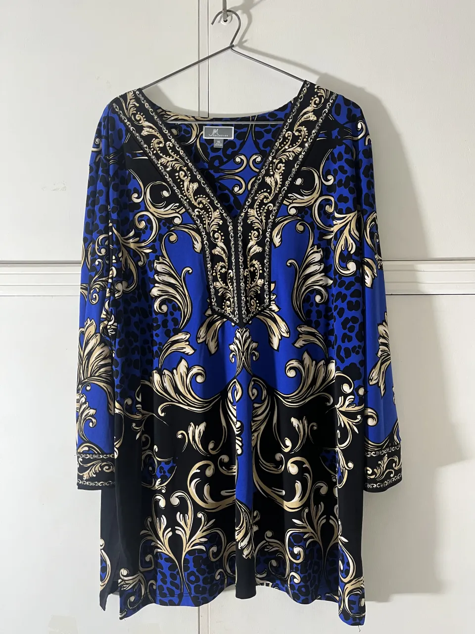 Remera estampada con motivos barrocos en azul, negro y dorado. Posee escote en V con detalles de pedrería dorada y un estampado de leopardo en las mangas y parte superior.