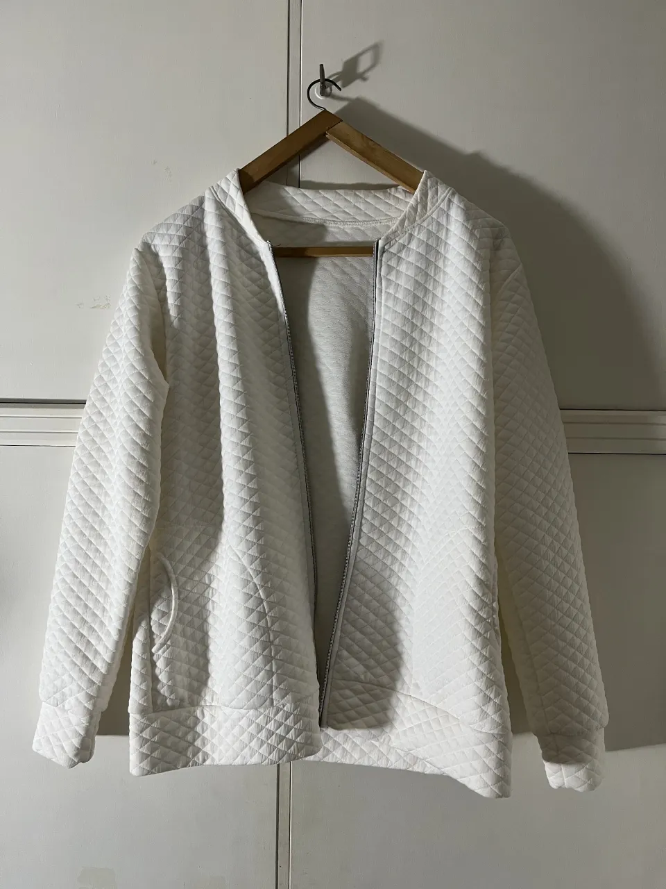 Campera blanca acolchada con rombos, cierre al frente y bolsillos laterales.