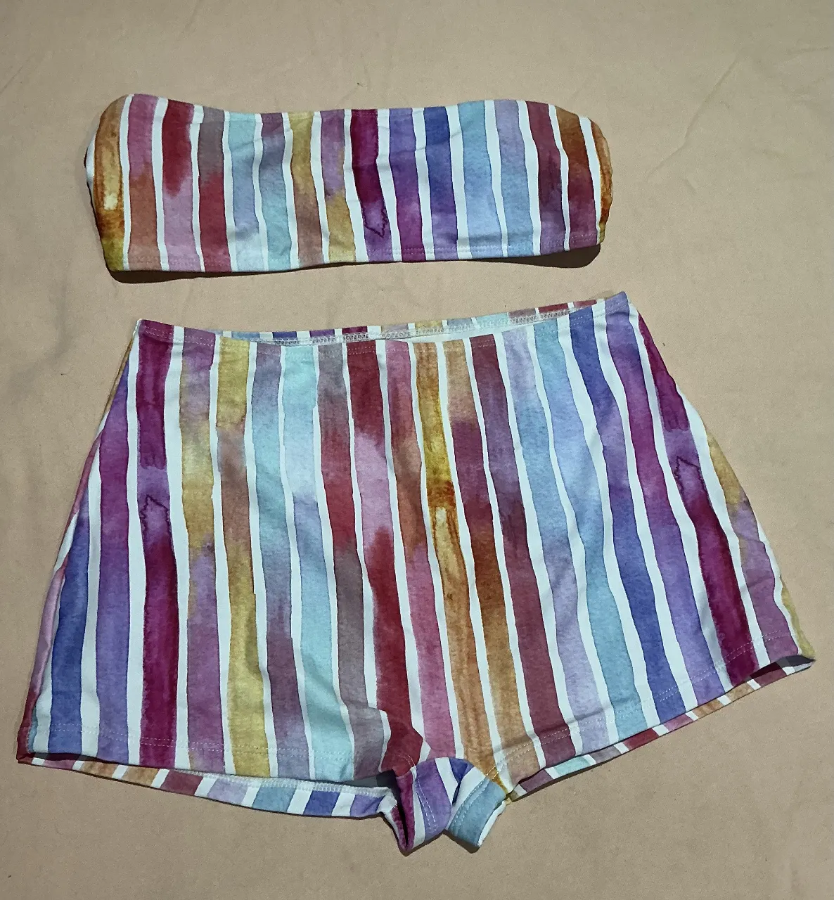 Conjunto de bikini de dos piezas con estampado de rayas verticales en acuarela. Incluye un top tipo strapless y un short tiro alto. Ideal para días de sol y playa.