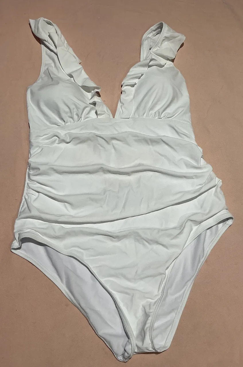 ¡Luce espectacular con este traje de baño entero blanco! Diseñado para realzar tu figura, cuenta con un favorecedor escote en V y delicados volados en los hombros que añaden un toque romántico. La parte del torso está fruncida estratégicamente para un efecto modelador y estilizado. Perfecto para disfrutar del sol y el mar con total confianza y estilo.