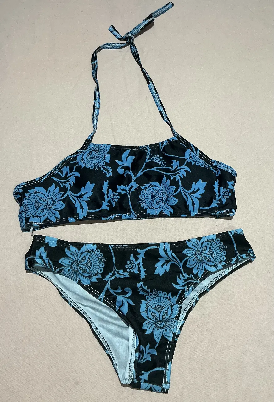 Bikini estampada con flores azules sobre fondo negro. Modelo de corpiño con tiras para atar en el cuello y bombacha estilo colaless. Ideal para disfrutar del sol y el mar.