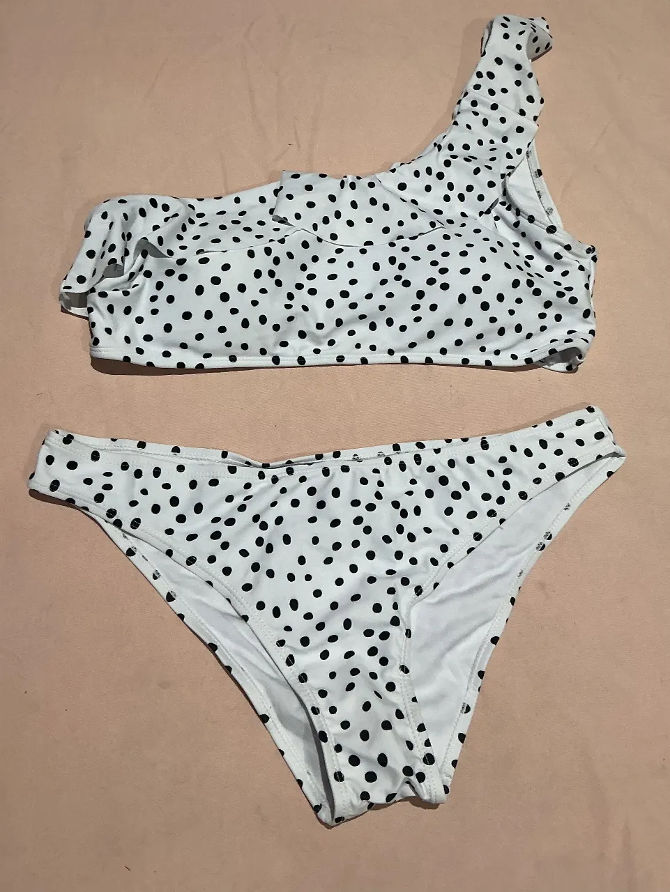 Bikini estampada con lunares blancos y negros. Modelo de una sola manga con volados y bombacha tiro alto. Ideal para disfrutar del sol y el mar con estilo.