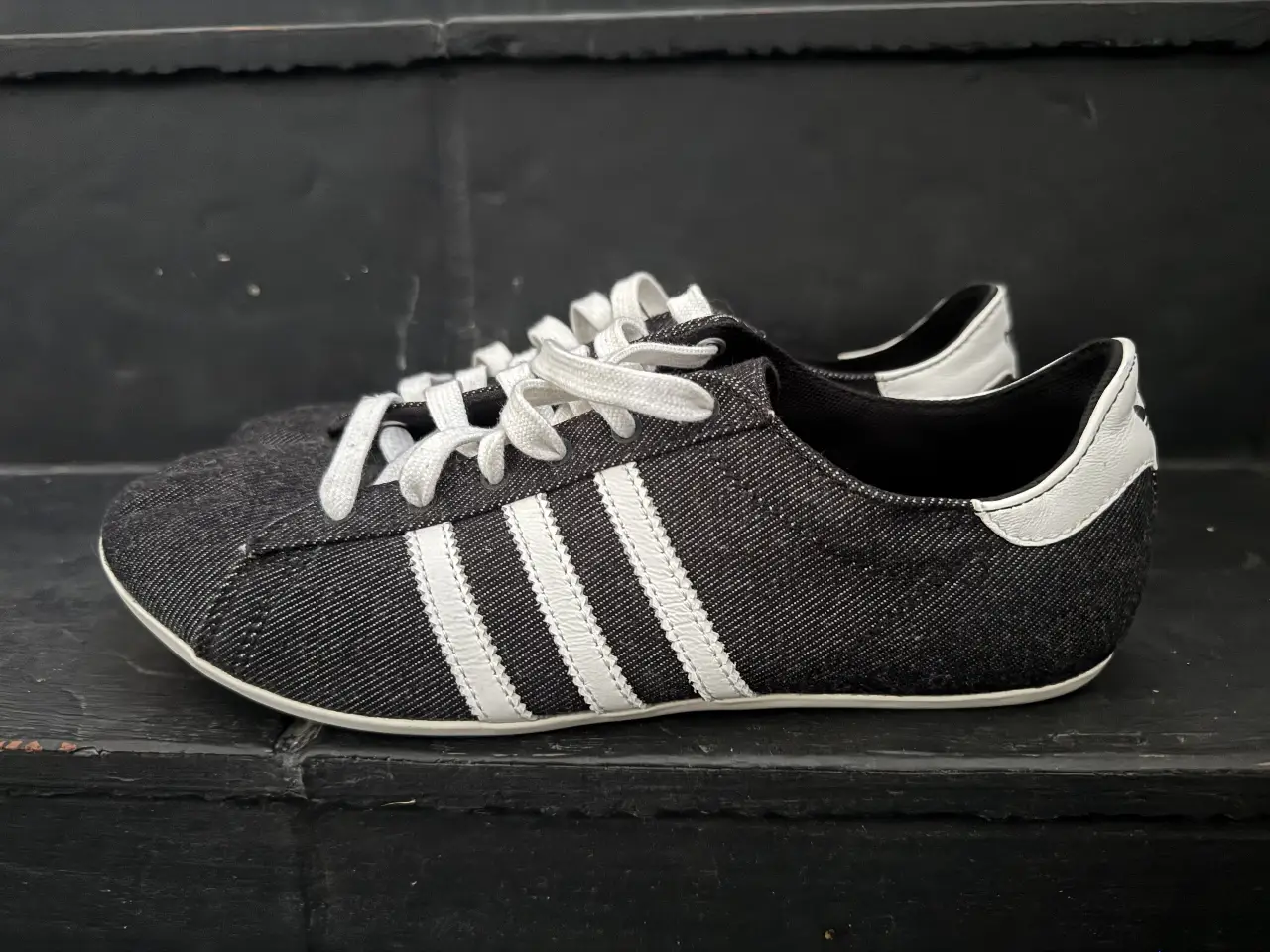 Zapatillas Adidas negras con detalles blancos. Diseño clásico con las tres tiras icónicas de la marca. Ideales para un look casual y cómodo.