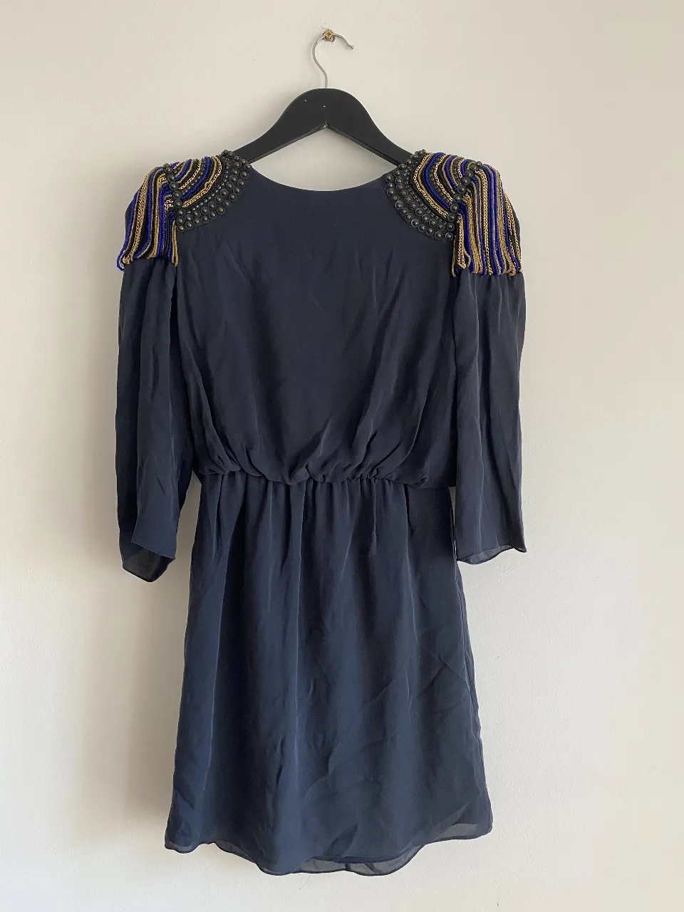 Vestido midi negro con detalles dorados en los hombros. Ideal para una fiesta o evento especial. Diseño elegante y sofisticado.