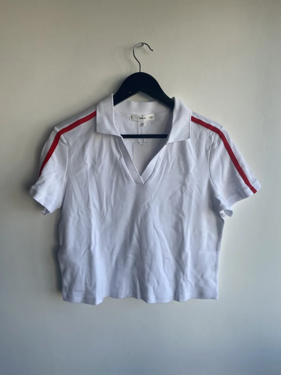 Remera blanca de manga corta con cuello polo y escote en V. Tiene una franja roja en cada manga.