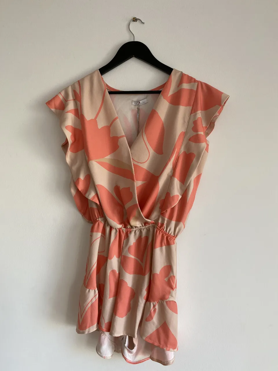 Vestido corto de mujer con estampado floral en tonos rosa y beige. Diseño con escote en V cruzado, mangas cortas con volados y cintura elastizada. Ideal para un look fresco y femenino.