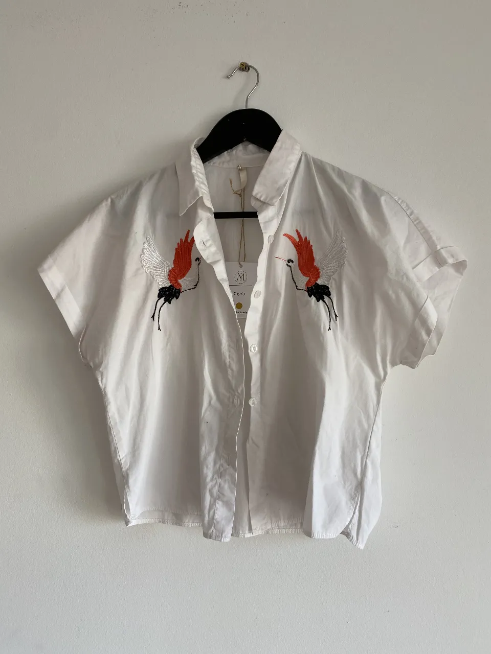 Camisa blanca con bordado de grullas en naranja y negro. Ideal para un look casual y fresco.