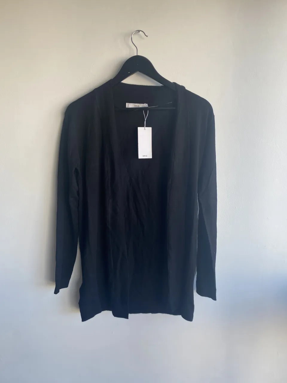 Cardigan negro de manga larga, abierto al frente. Tiene una etiqueta de marca visible.