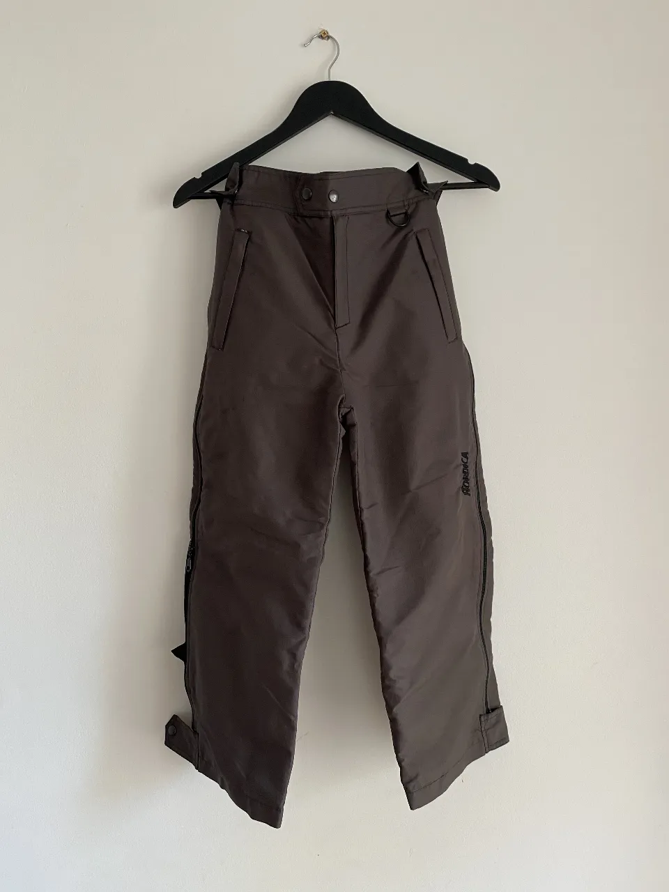 Pantalón de ski marrón, ideal para la nieve. Con cierres laterales y detalles de la marca. Perfecto para actividades de invierno.