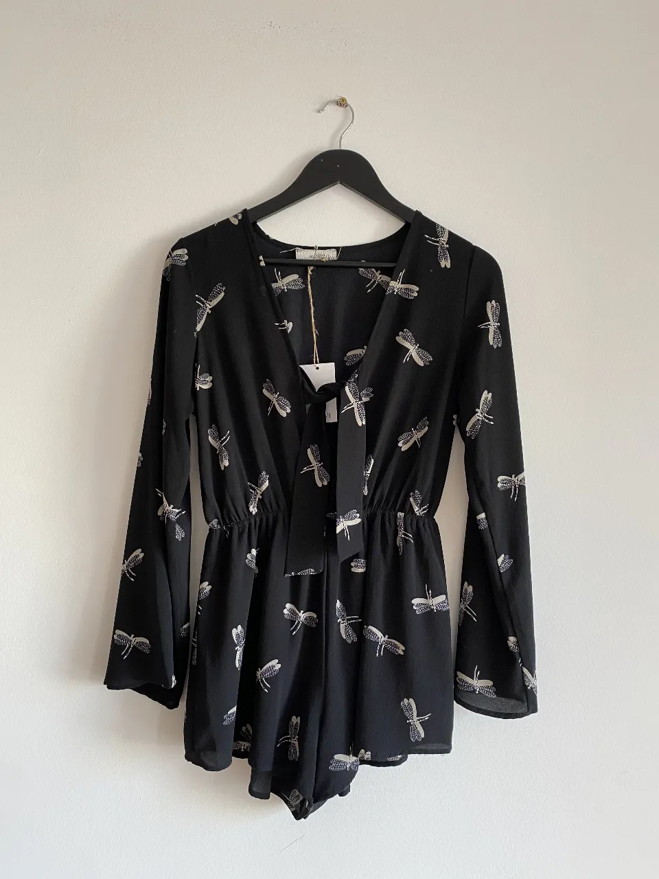 Mono largo negro con estampado de libélulas blancas. Tiene mangas largas con volados y un lazo en la cintura. Ideal para un look casual y fresco.