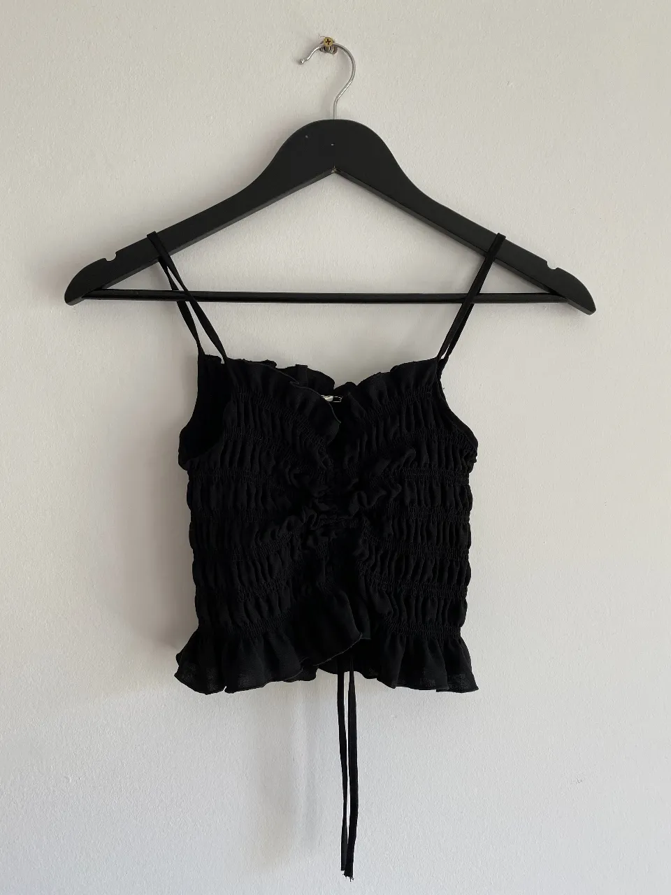 Top negro con breteles finos y detalle fruncido. Ideal para un look moderno y versátil.