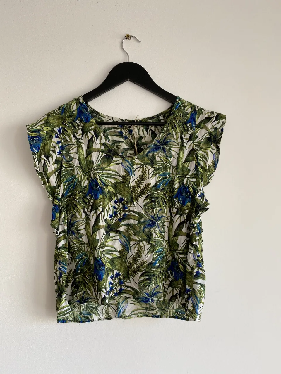 Blusa de mujer con estampado de hojas en tonos verdes y detalles azules. Ideal para un look fresco y casual.