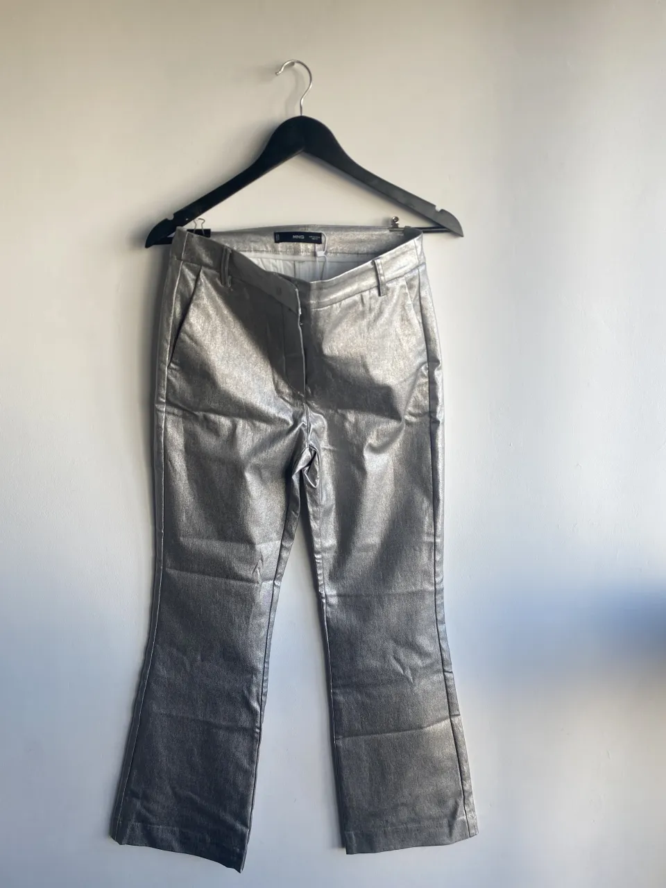 Pantalón plateado con brillo, corte al tobillo y bota ancha. Cierre y botón en la cintura.